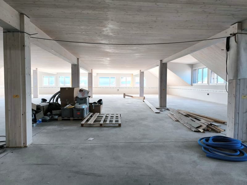 Under-construction room, concrete floor, wooden support beams, scattered storage boxes, large windows, pipes