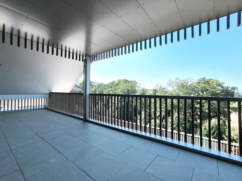 Large balcony, wooden railing, tiled floor, green trees outside, view of the hills