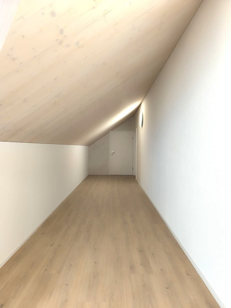 empty attic room with wooden floors, white walls, wooden ceiling