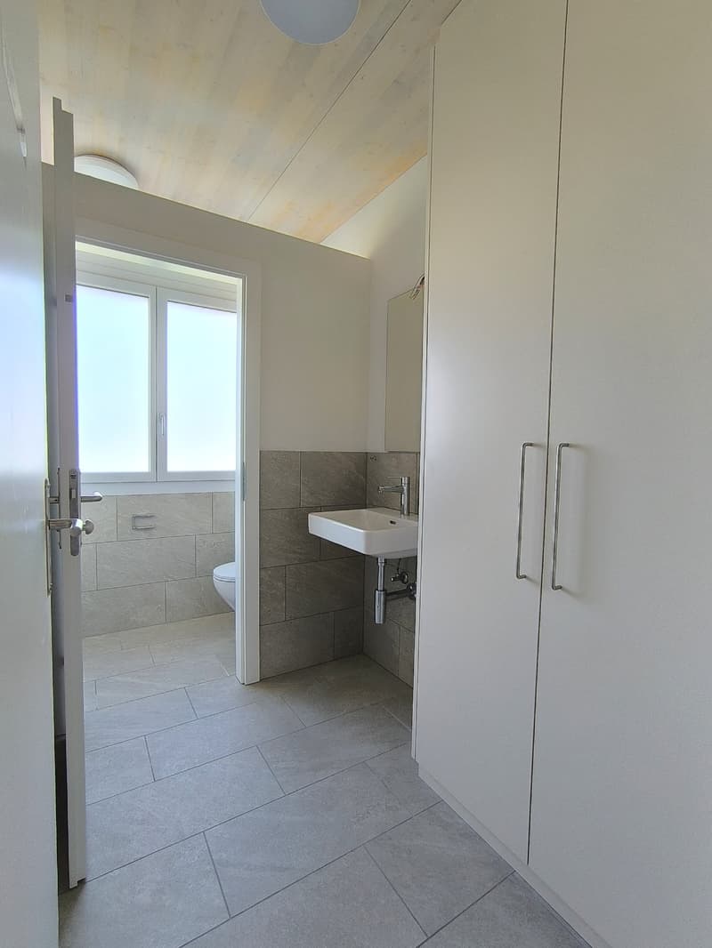 Modern bathroom with tiled floor, gray tiles on the wall, white sink, chrome faucet, white toilet, white storage cabinets, white door