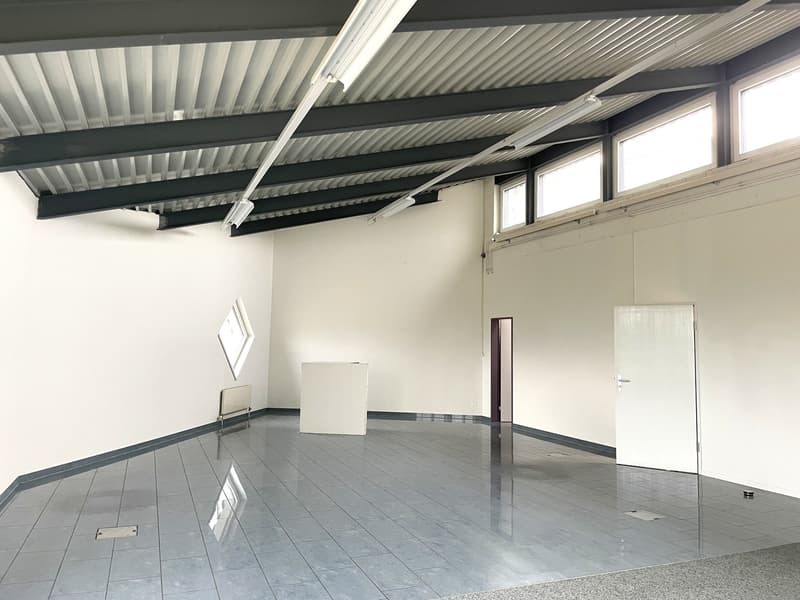 Empty room, tiled floor, metal beams on ceiling, white walls, windows, door, small white structure