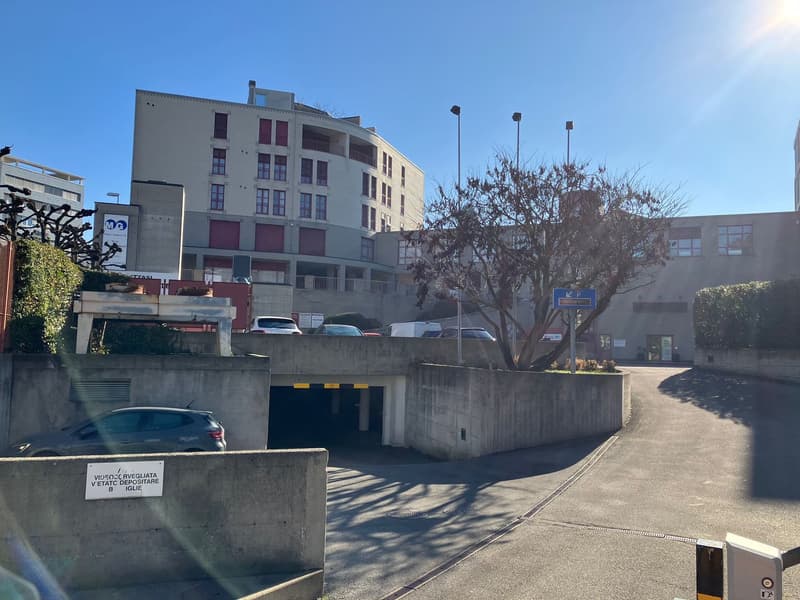Underground parking garage with limited view of cars parked, building in background, covered entrance