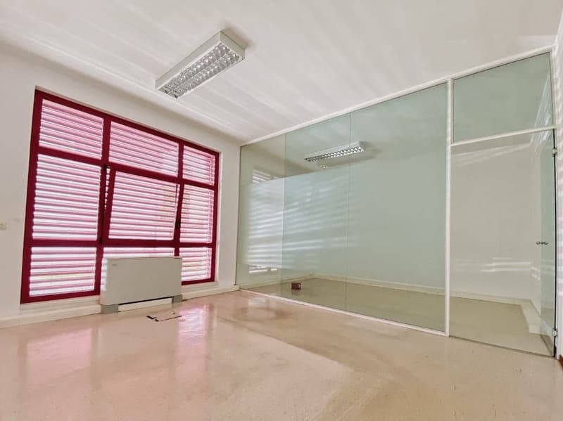 large room with glass walls and a window with red blinds, a white floor and ceiling