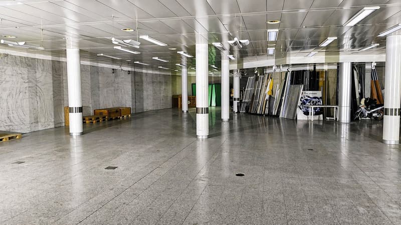 large open space, marble floor, white pillars, metal beams, ceiling lights, storage boxes, green screens