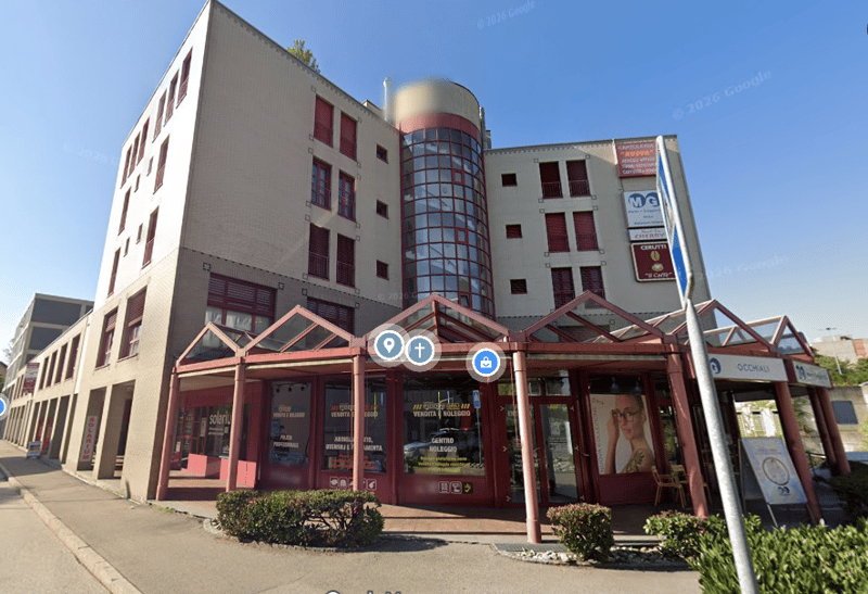A multi-story building with a modern architectural design, featuring glass windows, a red-framed entrance, and a glass wall with a spiral staircase visible inside.