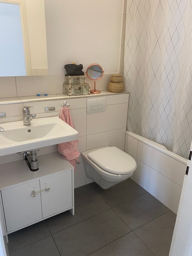 modern bathroom with white tiles, white sink, white toilet, mirror, pink towel, white cabinet, white shower curtain