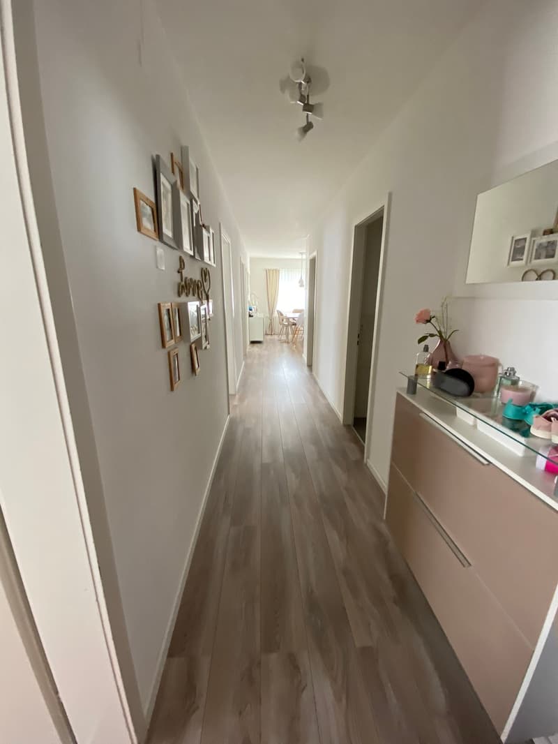 long hallway, wooden floor, white walls, framed pictures, mirror, cabinet, hallway light