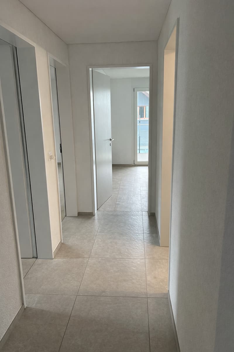 Empty hallway with tiled floor, white walls, and doors leading to different rooms.