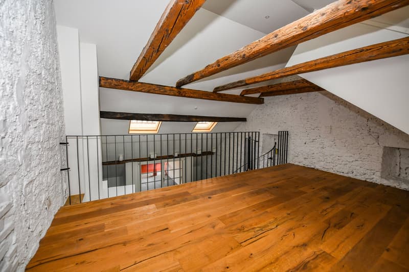 exposed wooden beams, hardwood floor, white walls, black railings, two skylights