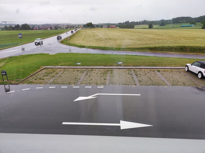 Aerial view of a parking lot with cars parked, a road with cars driving, and a grassy field in the background.