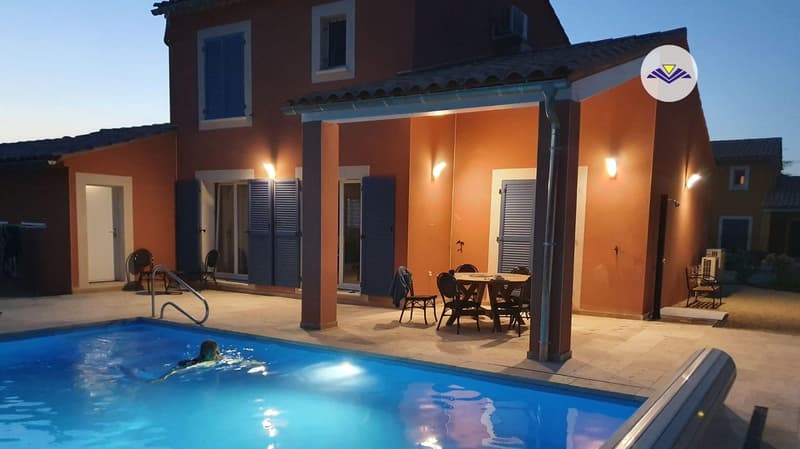 Two-story house with orange exterior, blue shutters, and a covered patio area. There is a swimming pool in the backyard that is illuminated at night.