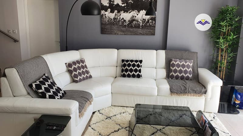 White leather sectional sofa, black and white patterned throw pillows, black and white area rug, black and white artwork on the wall, floor lamp, potted plant