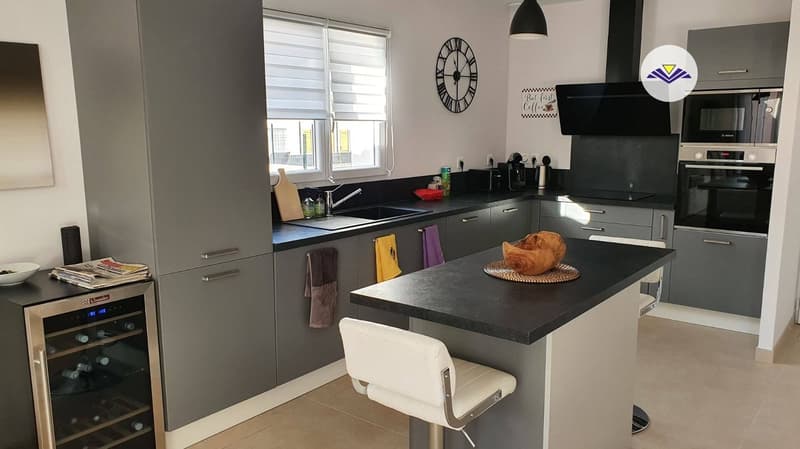 Modern kitchen with gray cabinets, black countertops, built-in oven, dishwasher, and a dining table with chairs