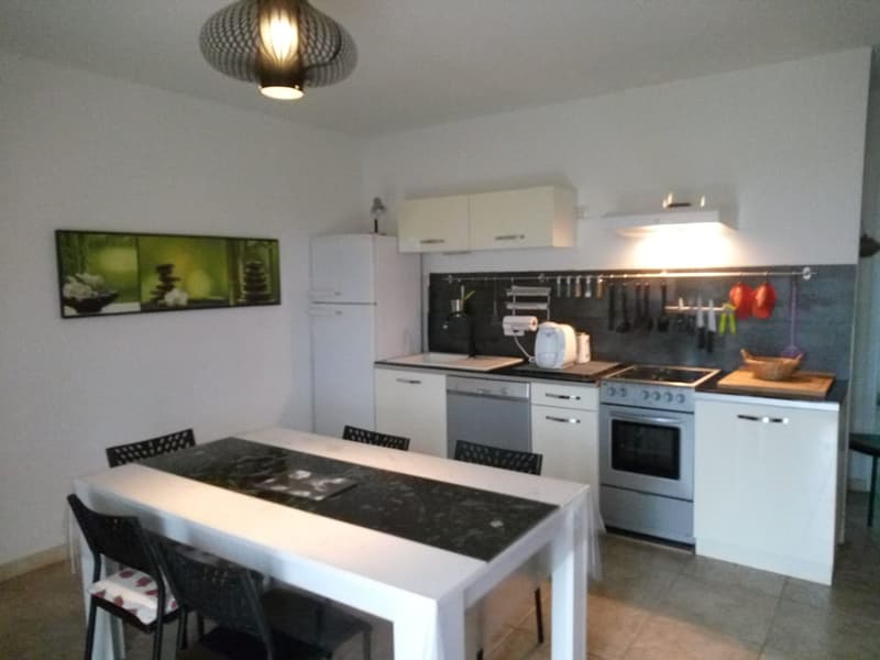 Modern kitchen with white cabinets, black countertops, stainless steel appliances including a dishwasher, and a dining table with chairs