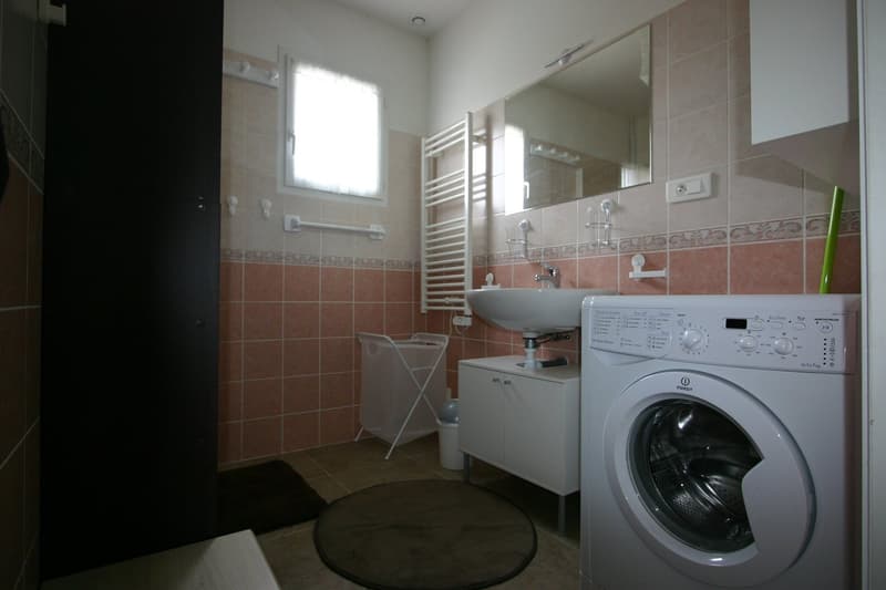Spacious bathroom with tiled walls, a sink, a towel rack, and a washing machine.