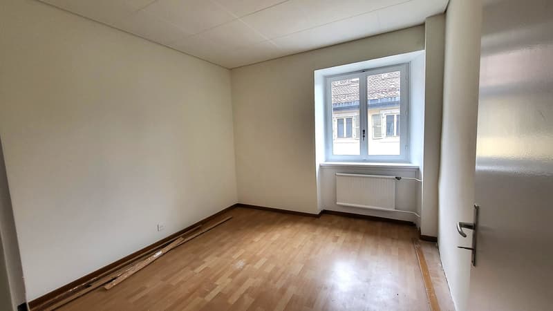 empty room with wooden floor, white walls, large window, radiator