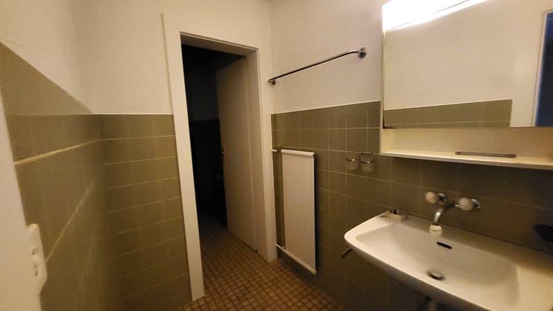 Bathroom with tiled walls and floor, a sink with a faucet, a mirror, and a towel rack mounted on the wall.