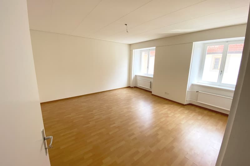 Empty room with wooden flooring, white walls, and windows.