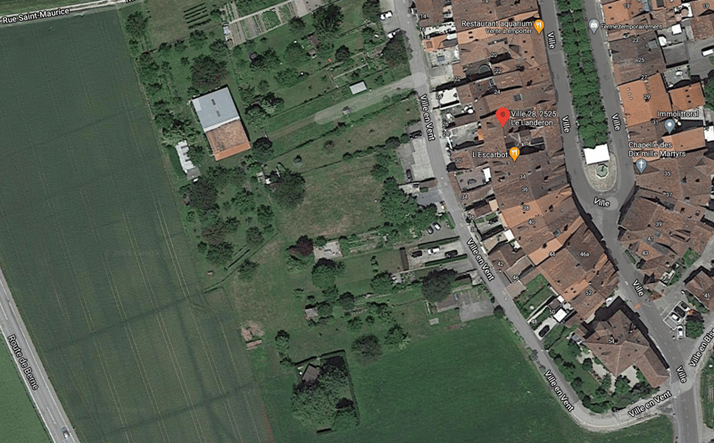 Aerial view of a residential area with buildings, green lawns, and a few parked cars.