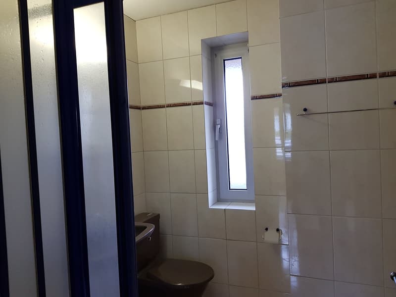 A bathroom with white tiles, toilet, sink, and a small window.