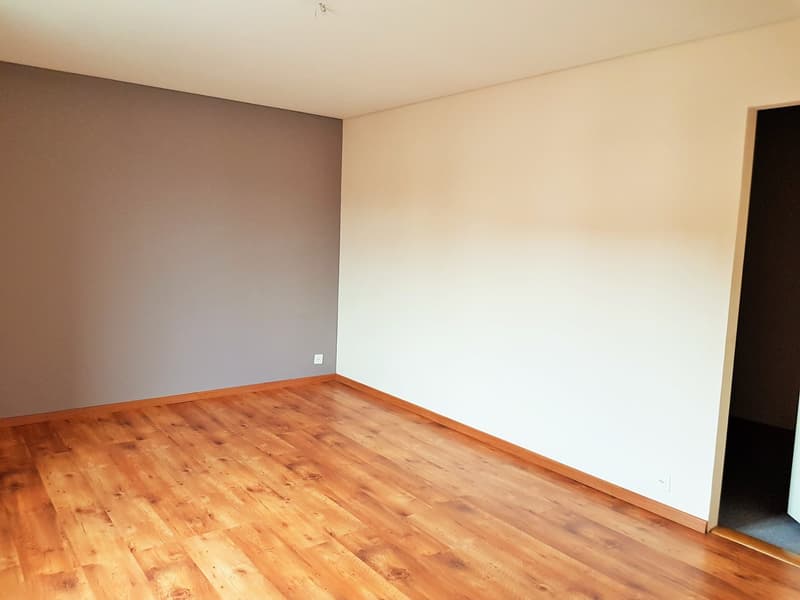 An empty room with wooden floors, white and grey walls, and power outlets on the wall