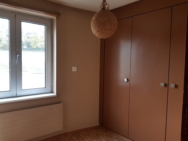 Empty room with beige walls, double window, large cabinet doors, hanging lamp, white radiator
