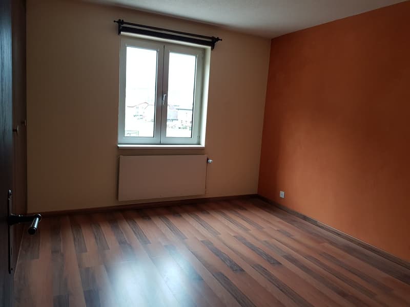 Empty room with window, heater, wooden floor, and walls painted in beige and orange
