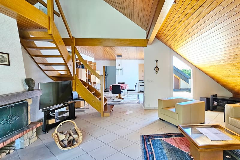 Fireplace, white tiled floor, wooden staircase, wooden ceiling, sofa, coffee table, TV, and basket of wood