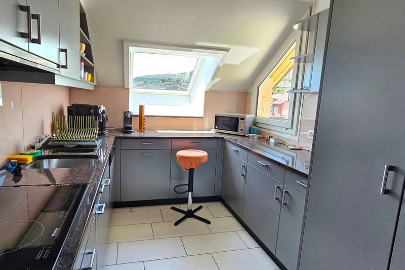 white floor tiles, gray cupboards, two sinks, stove top, orange stool, small microwave, small window