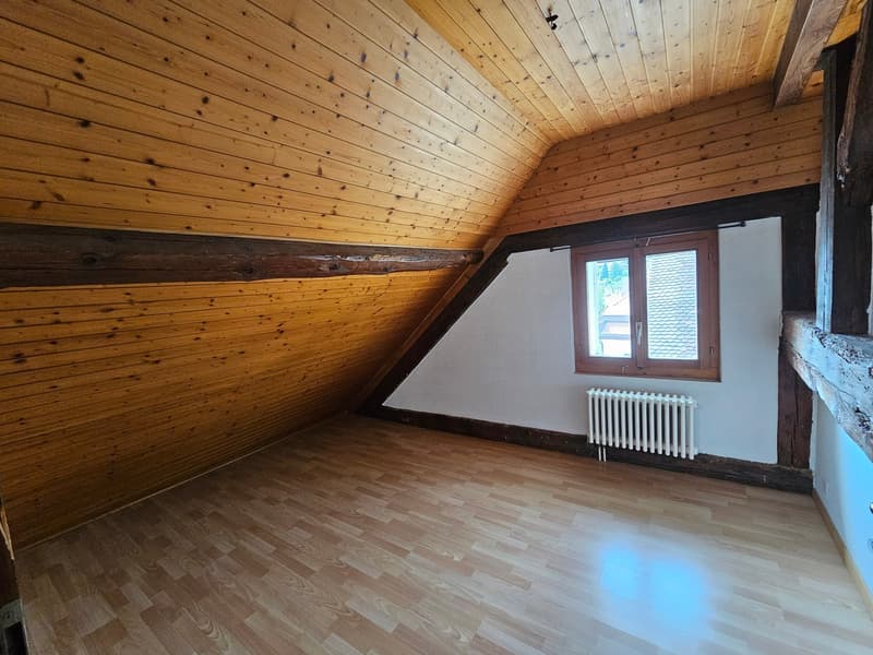 empty attic room with wooden ceiling, wooden floor, white wall, window, radiator
