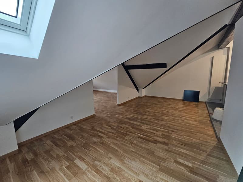 empty room, wooden floor, angled ceiling, attic windows, electrical outlets, bathroom sink, toilet paper