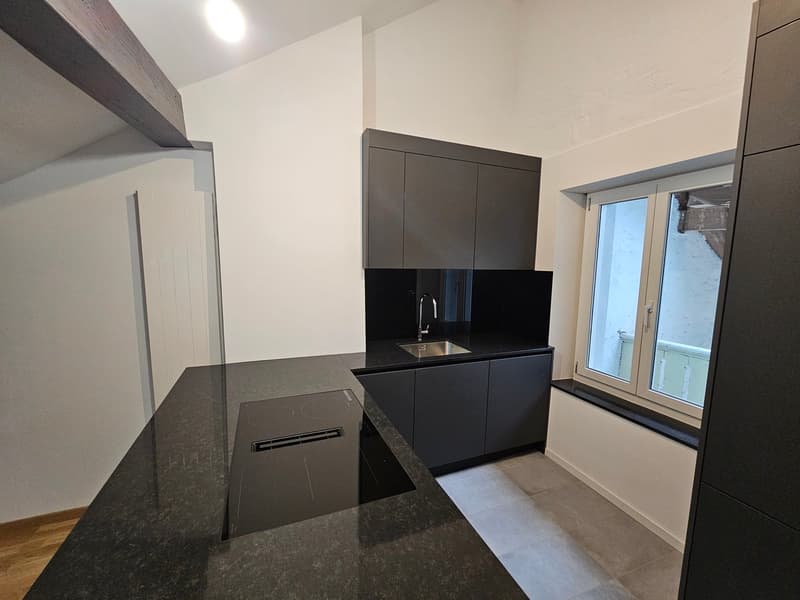 modern kitchen with granite countertop, stainless steel sink, black cabinets, induction cooktop, white walls, windows