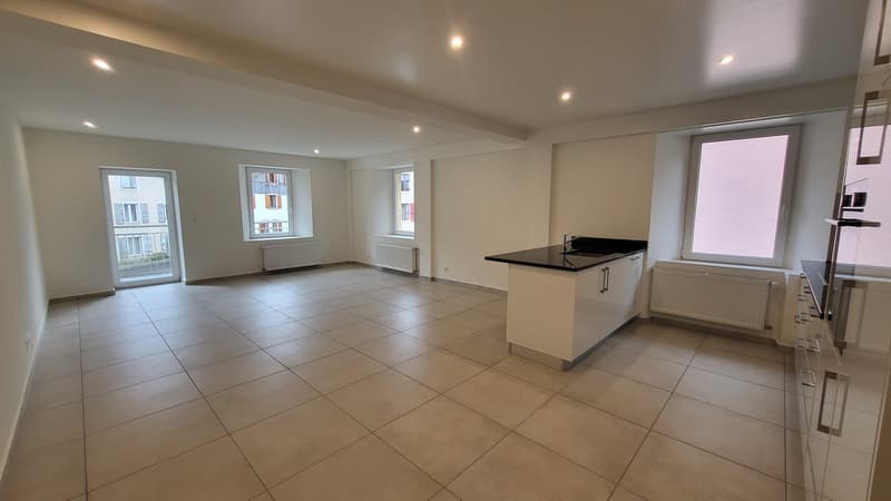 Empty kitchen with tiled floor, white cabinets, black countertop, sink, and windows