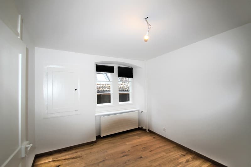 empty room, white walls, wooden floor, window with black blinds, white radiator