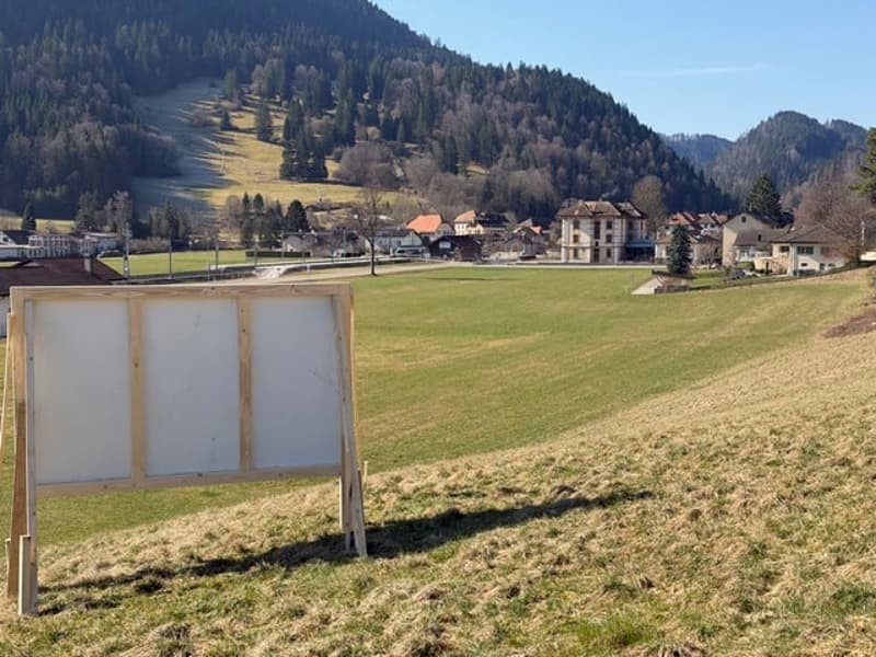 An open field, a whiteboard in the foreground, mountains and houses in the background