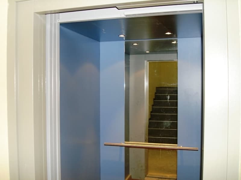 Blue elevator, silver handrail, white walls, stairs visible