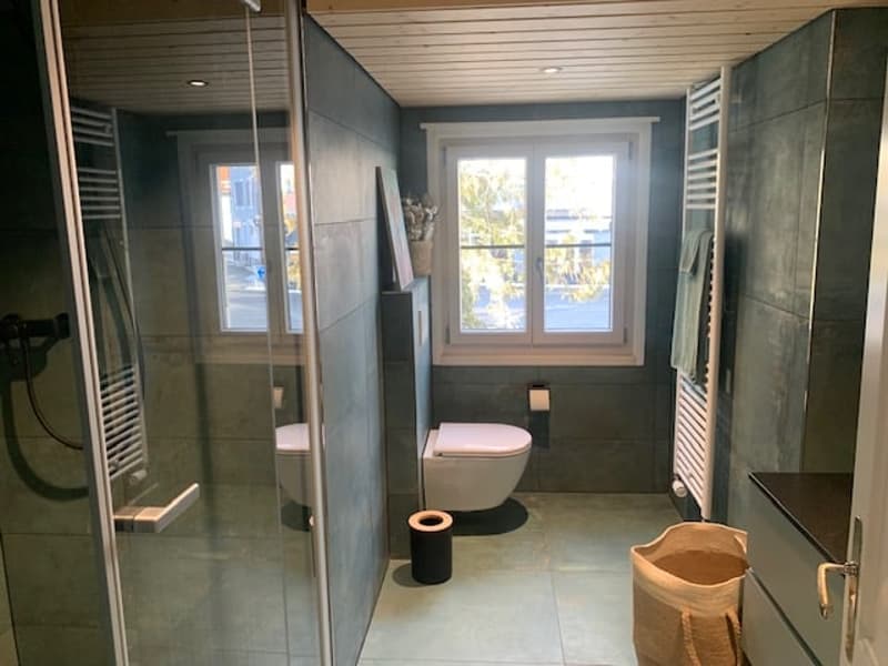 compact bathroom with toilet, shower, window, towel rack, trash bin