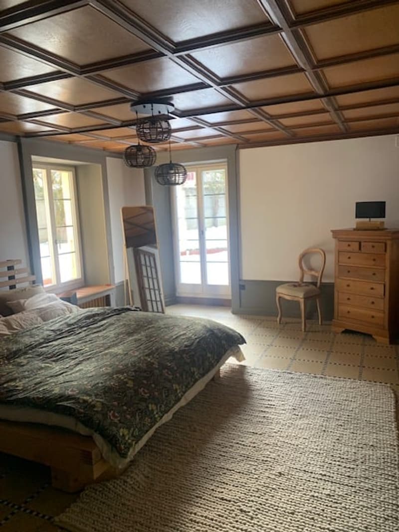 wooden bed, pillows, blanket, wooden chair, dresser, rug, windows, lamp, mirror