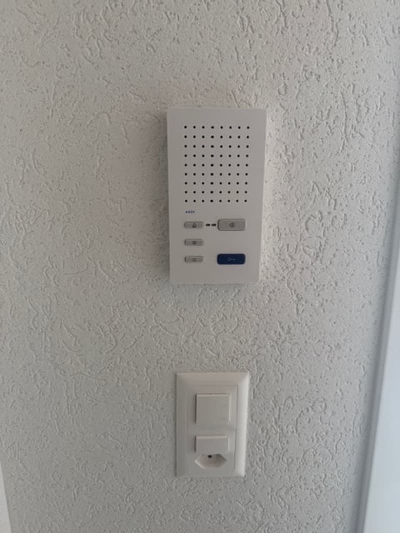 intercom, white with dots, 3 buttons on top, 1 button on the right, power socket next to it