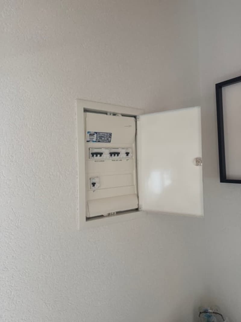 white wall, white metal box, open door, circuit breakers