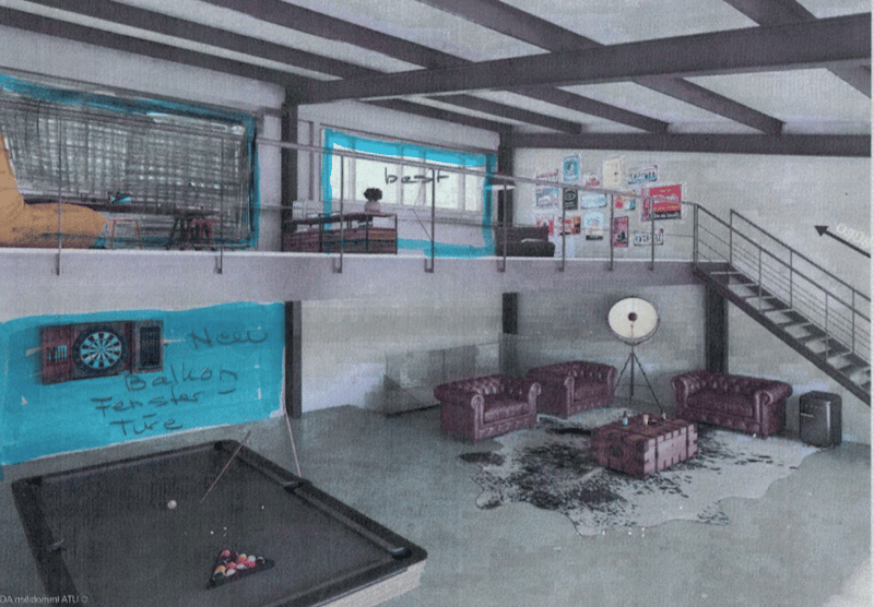 Furnished Room. A spacious, industrial-style room with exposed beams and concrete floors. Features include a large dartboard on the wall, a pool table, several purple leather sofas, a coffee table, and a floor lamp. The room has a lofted area with a stair