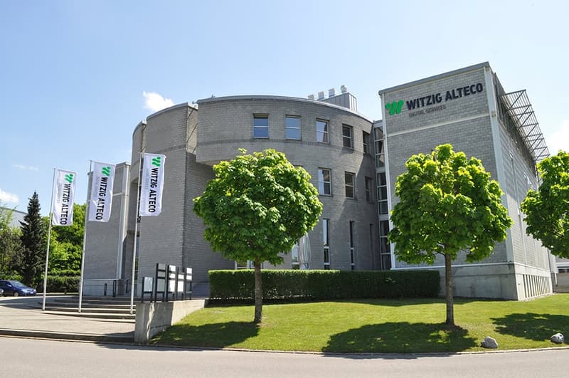 Modern office building with a curved facade, surrounded by a well-maintained lawn, trees, and flags.