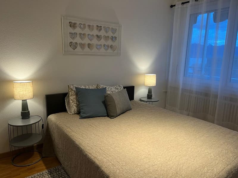 Bedroom with bed, two nightstands, lamps, rug, picture frame, curtains, radiator