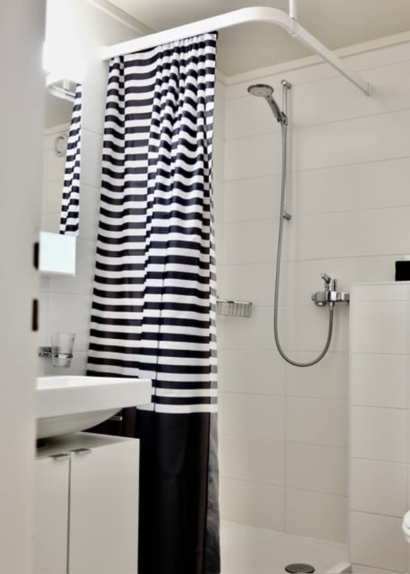 Bathroom. Modern bathroom with white tiles, a black and white striped shower curtain, a handheld showerhead, a sink with a mirror, and a small cup on the sink counter.