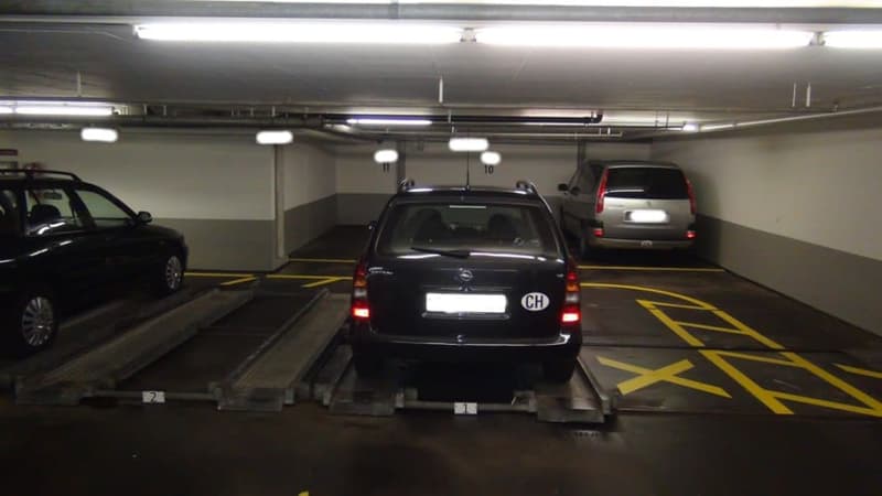 underground parking lot with 3 cars parked, yellow markings on the floor, white walls, fluorescent lights