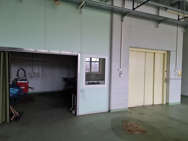 Warehouse room with steel door, window, trolley, white walls, shelves with pipes, hoses