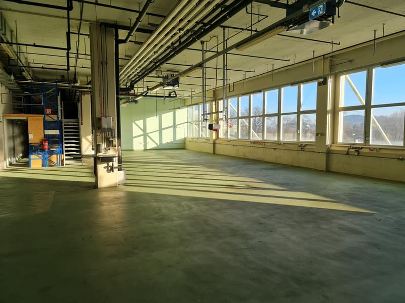 empty industrial space, concrete floor, large windows, exposed pipes, metal railing, fire extinguisher