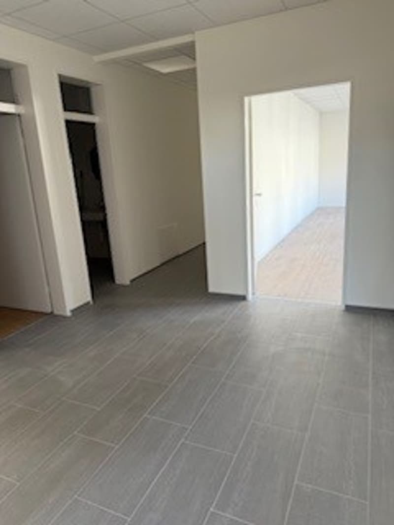 Empty room with tiled flooring, white walls, two open doors, and a small window on the left wall.