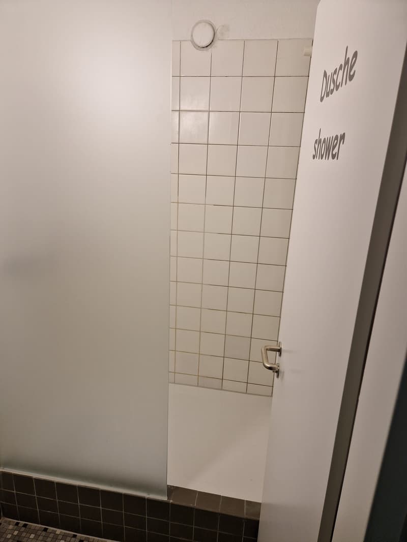 The image shows a bathroom with white tiled walls and a door labeled 'Dusche shower'.