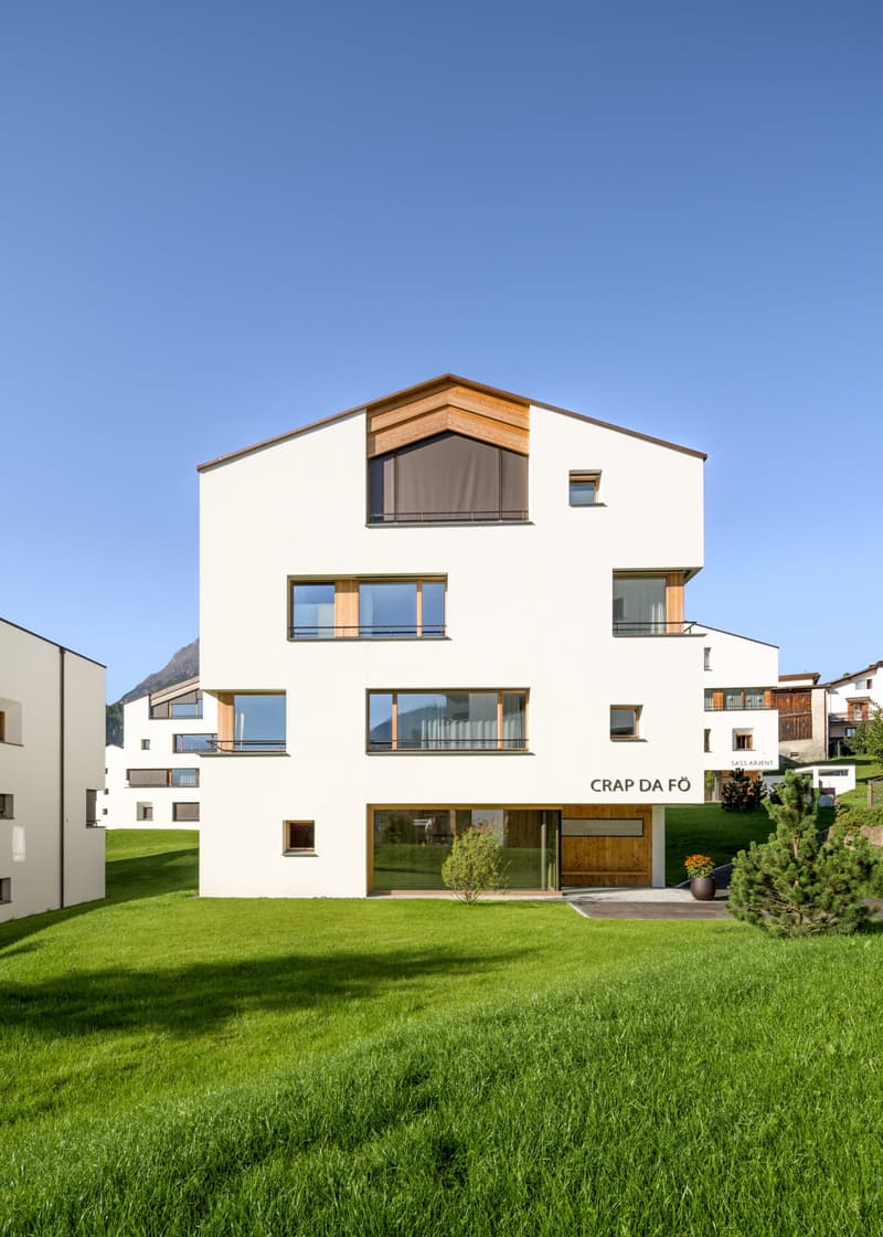 modern house, multiple windows, large glass doors, wooden trim, surrounded by green grass, mountainous background